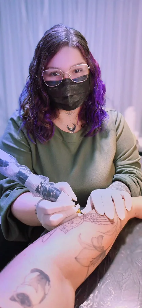 Stephanie Gama tatuando no estúdio em Curitiba, com máquina de tatuagem e luvas descartáveis