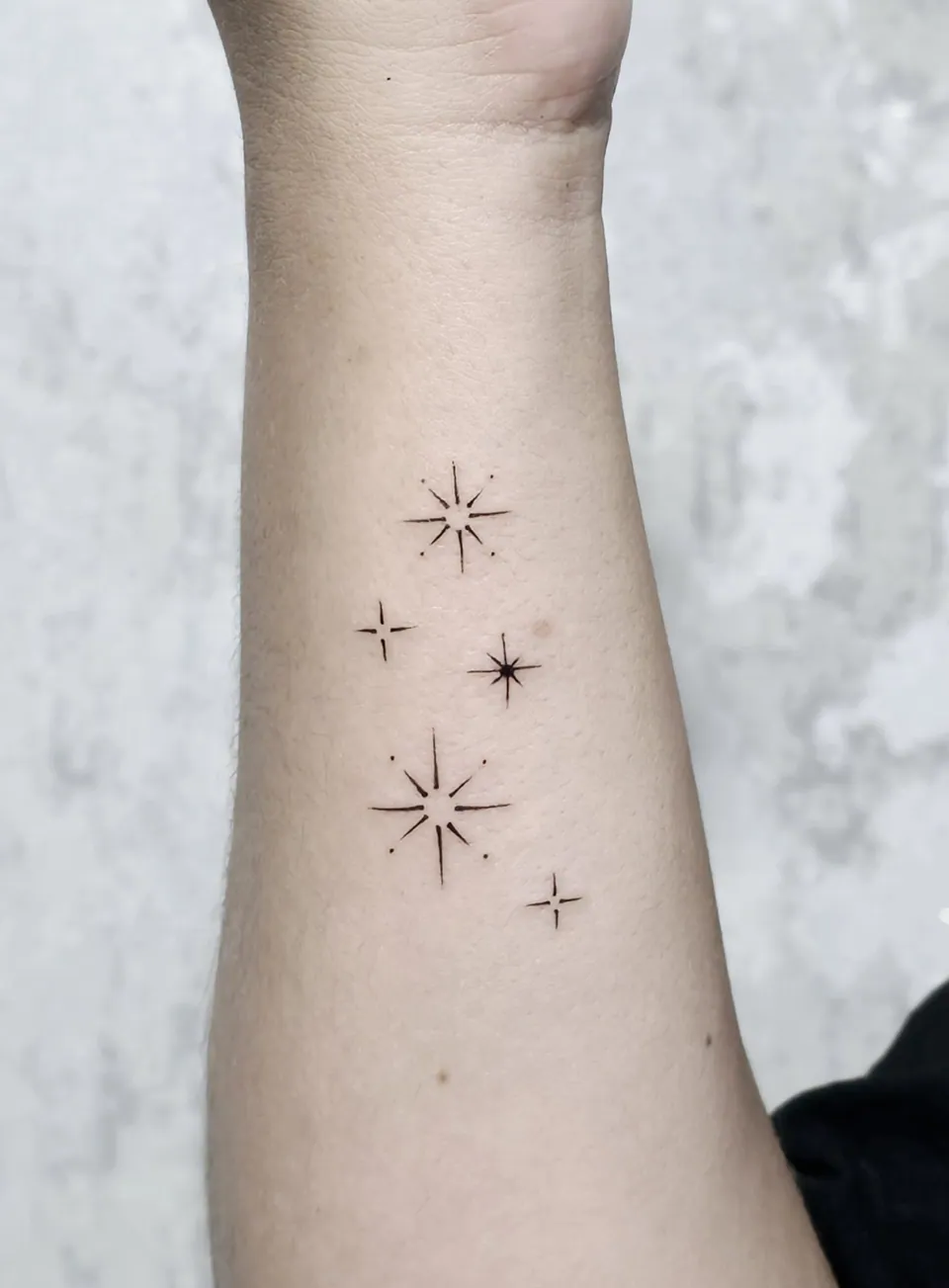 Estrelas minimalistas em traço fino no braço